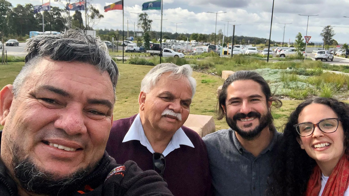 Justen, Steve, Pablo and Nicole take a group selfie in front of Australian, NSW, Aboriginal and Torres Strait Islander flags.