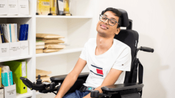 A person using a wheelchair smiles next to a bookshelf.