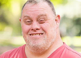 Leigh, a man with Down Syndrome, smiles at the camera.