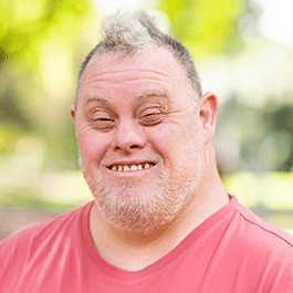 Leigh, a man with Down Syndrome, smiles at the camera.