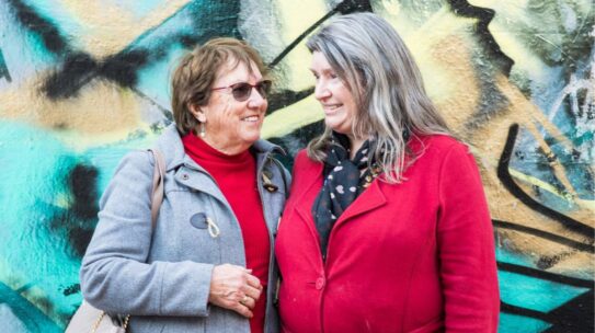 A mother and her daughter with intellectual disability smile while standing in front of a mural.