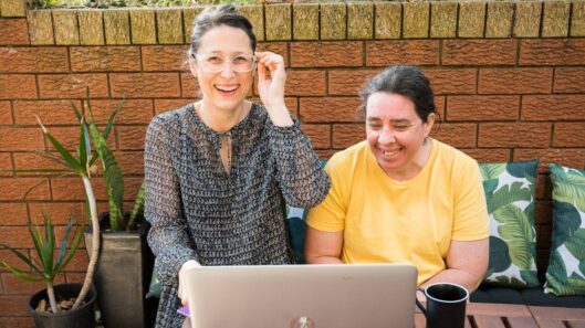 Two people work at a computer together while smiling.