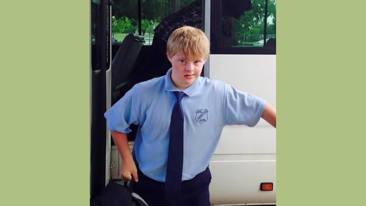 Finlay Browne, a young man with Down Syndrome, stands in his school uniform in front of an open bus door.