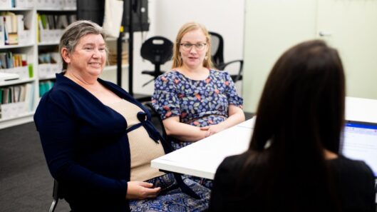 Three women meet around a table. One of the women has an intellectual disability.