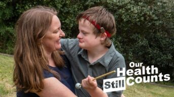 A mum and her son with Down syndrome embrace. The text Our Health Still Counts is to the side.