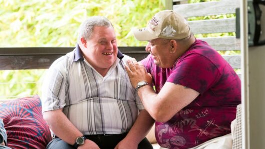 Two men with intellectual disability sit together and laugh.