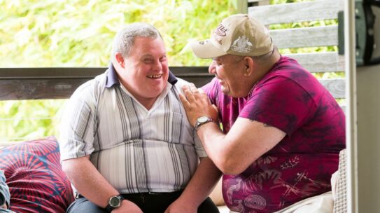Two men with intellectual disability sit together and laugh.