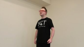 A young man with intellectual disability standing in a white room and singing.
