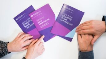 Hands holding and pointing at Disability Royal Commission pamphlets.