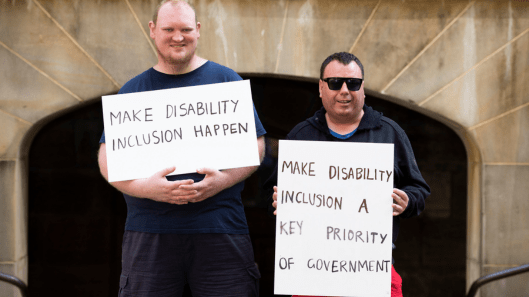 Two men with intellectual disability hold signs that say Make Disability Inclusion Happen and Make Disability Inclusion a Key Priority of US Government.