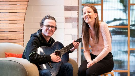 Two young people with intellectual disability smiling while one plays the guitar.